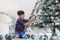 Child decorate the christmas tree with balls and ladder at home