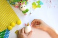 Child decorates an egg for Easter, makes a unicorn from an egg on a white table.