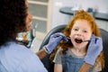 A child at dental clinic. Close up portrait of little child girl with red curly hair, sitting with open mouth in dental Royalty Free Stock Photo