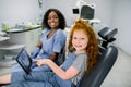 Child at dentist`s office. Little patient red haired girl, sitting in dentistry chair, looking at camera and pointing on