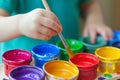 child dipping paintbrush into a palette of vibrant paint pots