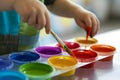 child dipping paintbrush into a palette of vibrant paint pots
