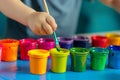 child dipping paintbrush into a palette of vibrant paint pots