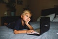 Child does homework , lying in bed using his laptop or skyping. Royalty Free Stock Photo