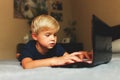 Child does homework , lying in bed using his laptop or skyping. Royalty Free Stock Photo