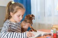 Child with dog reading book at home. Girl with pet sitting at window at read Royalty Free Stock Photo