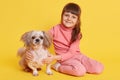 Child with dog sitting on floor isolated over yellow background, smiling toddler hugging Pekingese while sitting on floor, kid Royalty Free Stock Photo