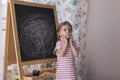 Child is drawing with pieces of color chalk on the chalk board. Girl is expressing creativity and looking at the camera Royalty Free Stock Photo