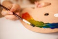 Child drawing rainbow by oil paint on wooden pallet