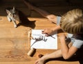 child draws contrasting shadows from skeleton of toy dinosaur while sitting on floor in company of his beloved kitten Royalty Free Stock Photo