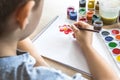 The child draws gouache on a white sheet and jars of paint are on the table. Hobbies and entertainment for children Royalty Free Stock Photo