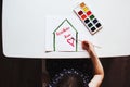 Child draws watercolors at a table drawing - a house with the words stay home