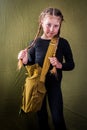 A child dressed in military style poses in a Studio. A little girl in a black leotard and a military bag over her shoulder stands