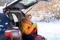 Child drinking hot chocolate or cocoa in sitting in black car at snowly winter day. Staycation tourism at winter time