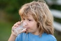 Child drinking water outdoor in park. Kid drinking. Close up portrait of boy drink water from glass in the garden. Royalty Free Stock Photo