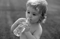 Child drinks water from a bottle while walking on grass field, baby health. Baby drinking water.
