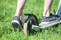 Child drives push stand-up scooter on green grass, close up rear view