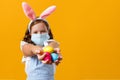 A child in the ears of an Easter bunny and in a protective medical mask on a yellow background. Royalty Free Stock Photo