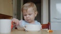 The child is eating in the kitchen. A small child learned to eat with a spoon by himself.