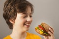 Child eats burger on grey background. Male child with hamburger