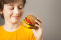 Child eats burger on grey background. Male child with hamburger