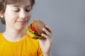 Child eats burger on grey background. Male child with hamburger