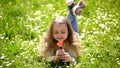 Child enjoy fragrance of tulip while lying at meadow. Girl with long hair lying on grassplot, grass background. Girl on