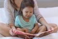 A child enjoying reading a book in bed with her mother