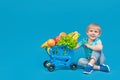 A child of European appearance, a blond boy, is sitting on the floor near a shopping trolley from a supermarket filled with Royalty Free Stock Photo