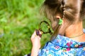 The child explores the grass in the meadow through a magnifying glass. Little girl exploring the flower through the magnifying