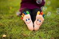 Child feet with painting smiles lying on green grass