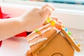 Child fingers placing candy balls and gummies on a gingerbread house roof with icing sugar as a creative and classic, seasonal