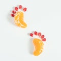 Child footprints made of two mandarin slices and pomegranate seeds on a white background. Creative minimal healthy food concept.