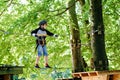 Child in forest adventure park. Kid boy in helmet climbs on high rope trail. Agility skills and climbing outdoor Royalty Free Stock Photo