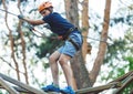 Child in forest adventure park. Kid in orange helmet and blue t shirt climbs on high rope trail. Agility skills Royalty Free Stock Photo