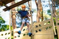 Child in forest adventure park. Kid in orange helmet and blue t shirt climbs on high rope trail. Agility skills Royalty Free Stock Photo