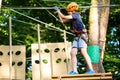 Child in forest adventure park. Kid in orange helmet and blue t shirt climbs on high rope trail. Agility skills Royalty Free Stock Photo