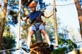 Child in forest adventure park. Kid in orange helmet and blue t shirt climbs on high rope trail. Agility skills and climbing Royalty Free Stock Photo