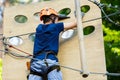 Child in forest adventure park. Kid in orange helmet and blue t shirt climbs on high rope trail. Agility skills Royalty Free Stock Photo