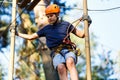 Child in forest adventure park. Kid in orange helmet and blue t shirt climbs on high rope trail. Agility skills Royalty Free Stock Photo