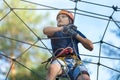 Happy child, healthy teenager in helmet enjoys activity in a climbing adventure rope park