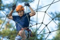 Child in forest adventure park. Kid in orange helmet and blue t shirt climbs on high rope trail. Agility skills Royalty Free Stock Photo