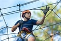 Child in forest adventure park. Kid in orange helmet and blue t shirt climbs on high rope trail. Agility skills Royalty Free Stock Photo