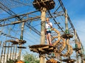 Child in forest adventure park. Kid in orange helmet and white t shirt climbs on high rope trail. Agility skills and climbing Royalty Free Stock Photo