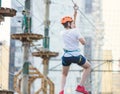 Child in forest adventure park. Kid in orange helmet and white t shirt climbs on high rope trail. Agility skills and climbing Royalty Free Stock Photo