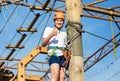 Child in forest adventure park. Kid in orange helmet and white t shirt climbs on high rope trail. Agility skills and climbing Royalty Free Stock Photo