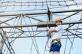 Child in forest adventure park. Kid in orange helmet and white t shirt climbs on high rope trail. Agility skills and climbing Royalty Free Stock Photo