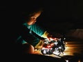 Child and garland in the dark. little child holds shiny christmas lights indoors close dark background. Portrait of a happy kid
