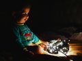 Child and garland in the dark. little child holds shiny christmas lights indoors close dark background. Portrait of a happy kid