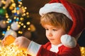 Child with garland lights at Christmas tree and fireplace on Xmas eve. It is miracle. Family with kids celebrating